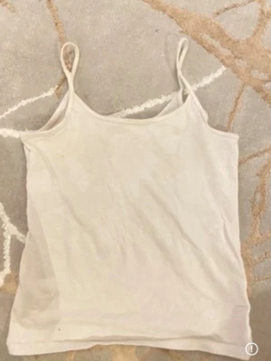 Vit enkel linneto - Säljer en basic vit linnetopp med tunna axelband och rak passform. Perfekt att styla lager på lager eller bära som den är. Materialet känns mjukt och lätt, vilket gör toppen skön att ha på sig under varma dagar.