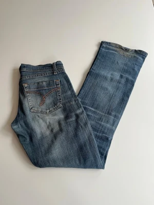 Blå bootcut jeans  - Snygga blå bootcut jeans med ljusa slitningar och kontrastsömmar på bakfickan. Klassisk femficksmodell med knapp- och dragkedjegylf. Perfekta för en avslappnad och trendig look.