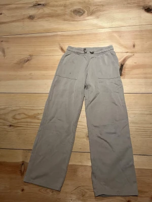 Beige mjukisbyxor med raka ben - Beiga mjukisbyxor med raka ben och resår i midjan samt dragsko. Byxorna har två stora fickor fram och två bakfickor. Perfekta för en avslappnad stil och tillverkade i mjukt material som känns skönt mot huden.