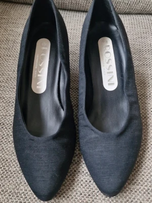 Svarta klackskor - Skorna är klädda i ett tyg som inte ligger limmat mot skon överallt (se bilder). Inget som jag tycker förstör utseendet men det är väl en smaksak. Inköptes innan livet kom emellan och jag fick inse att sneakers är smidigare 😂 Som ni ser på sulorna är de använda men endast vid ett par tillfällen. Tyget är lite skadat på höger klack (se bild). Stl 39.