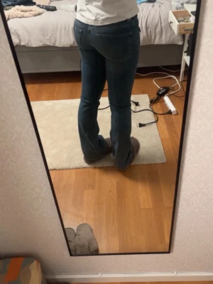 Blå bootcut jeans med fickor - Säljer ett par blå bootcut jeans med klassiska fickor fram och bak. Jeansen har en snygg tvätt och markerade sömmar längs benen. Passar perfekt till en avslappnad stil och är tillverkade i ett stretchigt denimtyg.