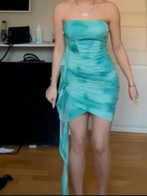 Turkos axelbandslös kortklänning - Säljer en snygg turkos axelbandslös kortklänning med knyt i sidan och draperad effekt. 