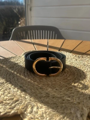 Svart bälte från Pieces med gulddetalj - Snyggt svart bälte från Pieces med en iögonfallande rundad guldfärgad metallspänne. Bältet är stilrent och passar perfekt till jeans eller kjol🤩