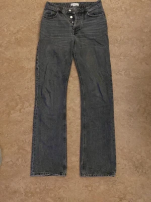 Mörkblå raka jeans med knappar - Säljer ett par mörkblå raka jeans med hög midja. Jeansen har klassiska fem fickor och är tillverkade i denim. 