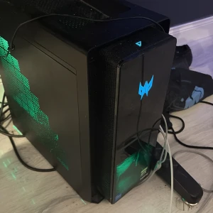 Acer Predator stationär gamingdator - Säljer en svart stationär dator från Acer Predator-serien med coola gröna och lila LED-lampor på sidorna. Chassit är i metall och plast med Predator-loggan framtill. Perfekt för gaming och tunga program tack vare sin kraftfulla design.