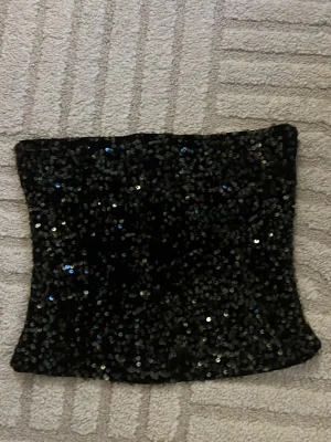 tubtopp - Snygg svart tubtopp täckt med glittriga paljetter. Perfekt för både fester och middagar. Toppen är axelbandslös och har en tight passform.  Materialet känns mjukt och stretchigt.