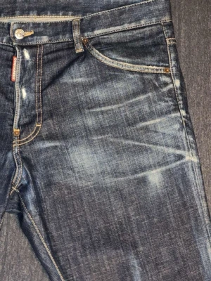 Blå jeans från Dsquared2 - Ordinarie pris 3999 säljer för 2,599          Säljer ett par blå jeans från Dsquared2 med snyggt sliten tvätt och kontrastsömmar. Klassisk femficksmodell med knappgylf och läderpatch bak i midjan. Jeansen har en rak passform och är tillverkade i bomull.