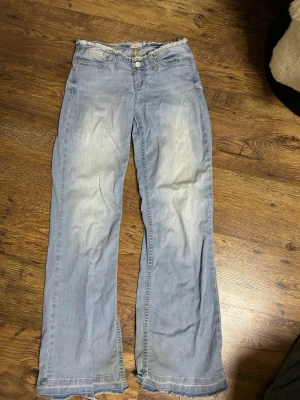 Ljusblå bootcut jeans med rå kant - Säljer ett par ljusblå bootcut jeans från Nelly (står it storlek men skulle säga s) med slitna detaljer och råa kanter nertill. Jeansen har klassisk femficksdesign och knappgylf. Materialet är mjukt denim i bomull och passformen är avslappnad med utsvängda ben.