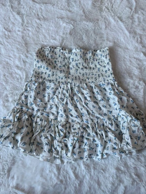 Vit blommig volangkjol/topp - Supersöt kort kjol/topp i vitt med små blå blommor och volangkant. Storlek XS, aldrig använd. 