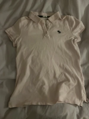 Ljus rosa pikétröja från Abercrombie & Fitch - Klassisk ljus pikétröja från Abercrombie & Fitch med korta ärmar, krage och knappar framtill. Tröjan har jag köpt secondhand och använt ett få tal gånger bara. Den är fin till en kjol eller ett par shorts i sommar💕💕