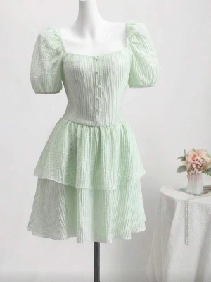Ljusgrön kort klänning med puffärm - Söt ljusgrön kort klänning med puffärmar, fyrkantig urringning och knappar framtill. Klänningen har dubbla volanger i kjolen och är tillverkad i ett lätt, strukturerat bomullstyg. Perfekt för sommarens alla tillfällen.