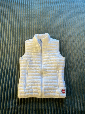 Vit dunväst från Colmar - Snygg vit dunväst från Colmar med quiltad design och hög krage. Västen har två dragkedjeförsedda fickor framtill och en liten Colmar-logga på nedre vänstra sidan. Perfekt att slänga över en hoodie eller tröja för extra värme.