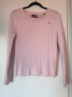 Ljusrosa kabelstickad tröja Gant - Supersnygg ljusrosa kabelstickad tröja från Gant med rund halsringning och diskret logga broderad på bröstet. Tröjan har långa ärmar och ribbade muddar vid ärmslut och nederkant. Perfekt för dig som gillar klassisk och stilren look. Tröjan är i storlek 158/164 men sitter som en xs skulle jag säga. 💕 Lappen har lossnat på ena hörnet, men det är inget som syns och går enkelt att sy fast😊
