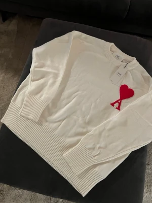 Vit stickad tröja från Ami Paris - Vit stickad tröja från Ami Paris med rund halsringning och ribbade muddar. Tröjan har en clean och modern look, perfekt för dig som gillar stilrena detaljer.