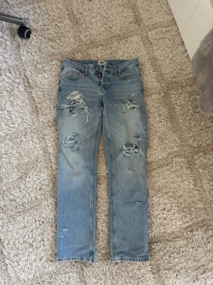 Ljusblå slitna jeans från lager 157 - Säljer ett par ljusblå jeans från lager 157 med raka ben och flera slitningar framtill för en trendig, avslappnad look. Klassisk femficksmodell och knappgylf. Hålen har jag klippt själv och det är snyggt att ha strumpbyxor under! Modellen på jeansen heter icon