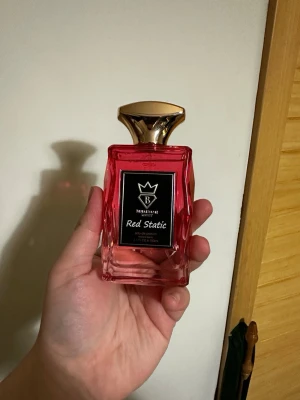 Bujairami Red Static (inspirerad av Dior Rouge Trafalgar Esprit De Parfum) - Red Static | Eau De Parfum 100ml | av Bujairami  En livfull och passionerad doft som blandar saftiga frukter med romantiska blommor, vilket skapar en energisk och fängslande aura.  Doftnoter:  Toppnoter: Körsbär, Rosépeppar  Mellannoter: Bulgarisk ros, Turkisk ros  Basnoter: Röda frukter
