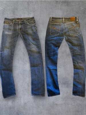 Vintage Nudie Jeans - Säljer ett par klassiska blå jeans från Nudie Jeans i rak modell. Jeansen har snygga slitningar, fem fickor och kontrastsömmar. Tillverkade i slitstarkt denim med cool vintagekänsla. Perfekta för en avslappnad och trendig look. Selvage jeans, bara och ställa frågor!