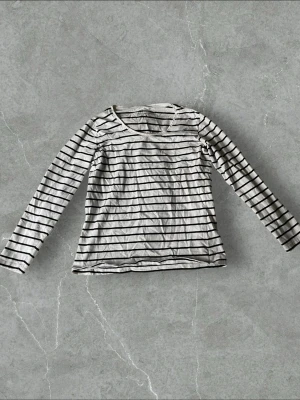 Randig långärmad topp från H&M - Klassisk långärmad topp från H&M Basic i vitt med svarta horisontella ränder. Tillverkad i mjuk bomull med rund halsringning och normal passform. Perfekt att styla med jeans eller kjol för en enkel och snygg look.