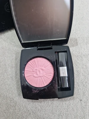 Chanel Coco Code rosa rouge - Chanel Coco Code Harmonie de Blush i en snygg rosa nyans. Kommer i en elegant svart dosa med spegel och tillhörande borste. Rouget har ett pressat Chanel-logomönster och ger en fräsch, naturlig look till kinderna.
