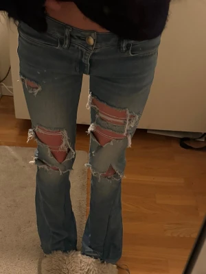 Blå slitna bootcut jeans - Säljer ett par ljusblå bootcut jeans med stora slitningar och hål på båda benen. Har sytt dom bootcut själv🩵osäker på storleken men midjemåttet är 34cm rakt över och innerbenslängden 71cm🩵
