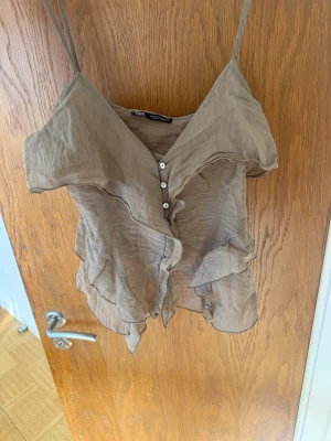 Söt volang topp med knappar💕 - Säljer en linnetopp med tunna axelband, v-ringning och dekorativa volanger framtill. Toppen har små knappar längs bröstet och ett lätt, luftigt material😊