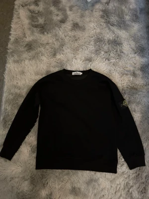 Stone Island tröja  - Säljer en svart sweatshirt från Stone Island med klassisk rund hals och lång ärm. Tröjan har den ikoniska Stone Island-loggan på vänster ärm och är tillverkad i mjukt bomullsmaterial. Enkel och stilren design som passar till det mesta.