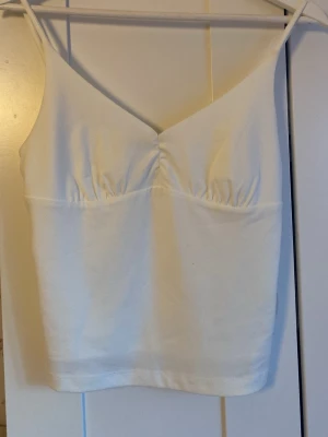 Vit croppad linnetopp med smala band - Snygg vit linnetopp med smala axelband och lätt rynkade detaljer vid bysten. Toppen är croppad och har en enkel, stilren design som passar perfekt till jeans eller kjol. .