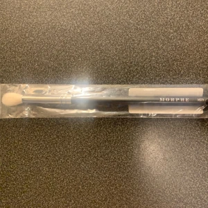Morphe M573 ögonskuggsborste - Säljer en Morphe M573 ögonskuggsborste med svart skaft och vita, fluffiga borst. Perfekt för att blenda ögonskugga och skapa mjuka övergångar. Borsten har ett stilrent utseende och ligger skönt i handen. Kommer i originalförpackning.