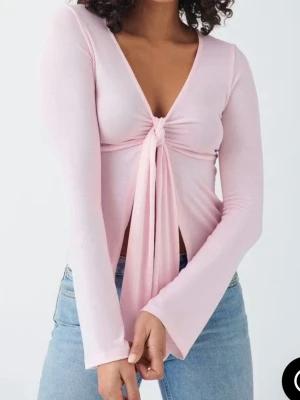 Ljusrosa omlottopp med knyt från Gina Tricot  - Trendig ljusrosa topp med lång ärm och djup v-ringning. Toppen har ett snyggt knyt framtill som ger en omlottkänsla och är croppad i modellen. Perfekt att styla med höga jeans för en cool look. 