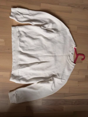Vit stickad tröja med rund hals - Klassisk vit stickad tröja med rund hals och långa ärmar. Tröjan har en enkel och stilren design med ribbade muddar vid ärmslut och nederkant. Perfekt att matcha med jeans eller kjol för en clean look.