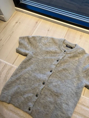 Grå kortärmad kofta från Gina Tricot - Mysig grå kofta från Gina Tricot med korta ärmar och knappar nedtill. Super skön och funkar super bra nu till våren. 