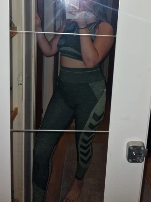 Träningsset - Snyggt grönt träningsset från Hummel med sport-bh och höga tights. Setet har mönstrade detaljer i ljusare grönt och är tillverkat i stretchigt funktionsmaterial som andas. Perfekt för gymmet eller löpning. Storlek M/L då de är stretchiga