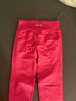Rosa tights från DFYNE - Dags att lysa upp gymmet! 💖 Säljer dessa supersnygga och populära DFYNE seamless leggings i en fantastisk rosa färg. Storlek Extra Small (XS). Om du älskar DFYNE och vill ha en färg klick i din träningsgarderob, är dessa för dig! Tightsen har den välkända och smickrande scrunch butt-designen (som syns tydligt på bild 1 och 5), vilket ger en fantastisk form. Materialet är DFYNEs klassiska mjuka, stretchiga och helt knäböjssäkera (squat-proof) tyg. Hög midja som sitter bekvämt och på plats under h