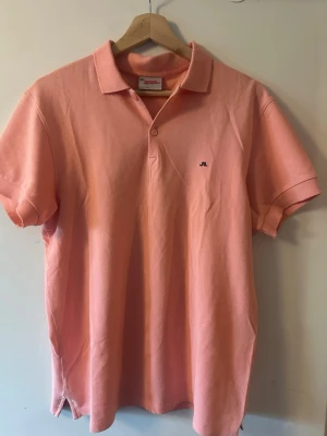 Ljusrosa pikétröja från J.Lindeberg - Säljer en ljusrosa pikétröja från J.Lindeberg med klassisk krage och korta ärmar. Tröjan har en liten broderad logga på bröstet och är tillverkad i mjuk bomull. Perfekt för en avslappnad men stilren look.