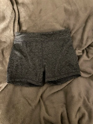 Mörkgrå träningstights-shorts - Säljer ett par mörkgrå, tighta träningstights-shorts från ICANIWILL. De har hög midja och är tillverkade i ett stretchigt syntetmaterial som passar perfekt för gymmet eller löpning. Snygg melerad look och diskret logga bak.