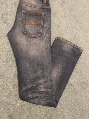 Nudie Jeans  - Säljer ett par blå jeans från Nudie Jeans med klassiska orange sömmar och broderad bakficka. Jeansen har en tvättad look och raka ben. Perfekta för dig som gillar en avslappnad men ändå stilren stil. Inga tecken på användning. Sjukt bra passform! Hör av er vid minsta fundering!