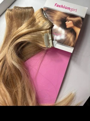 Blonda clip-on löshår från Fashiongirl - Snyggt blont löshår med clip-on från Fashiongirl. Håret är långt och vågigt, perfekt för att snabbt fixa en fylligare frisyr. Clipsen är smidiga att sätta i och ta ur. Ordinarie pris 300kr