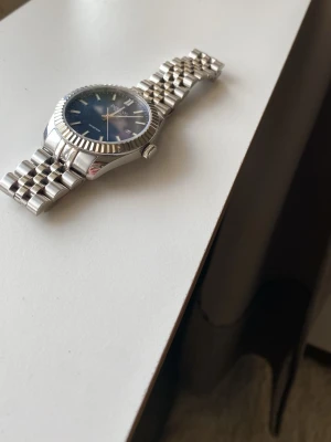 Dissing klocka med blå urtavla - Stilren klocka från Dissing med blå urtavla och datumvisning. Klockan har ett klassiskt armband i silverfärgat rostfritt stål och markerade index. Perfekt accessoar för dig som gillar en tidlös look.