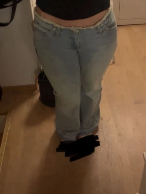 Ljusblå bootcut jeans med rå kant - Säljer ett par ljusblå bootcut jeans med låg midja och rå, fransig kant upptill och nertill. Jeansen har klassisk femficksmodell och är tillverkade i denim med lätt slitningar framtill. Perfekta för en avslappnad och trendig look.