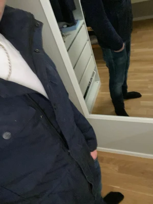 Mörkblå parkajacka från Lindbergh - Säljer en mörkblå parkajacka från Lindbergh med hög krage och flera praktiska fickor framtill. Jackan har dragkedja och knappar, samt en klassisk parkamodell som passar perfekt till jeans. Materialet känns slitstarkt och jackan har långa ärmar. Dragkedjan i mitten är sönder