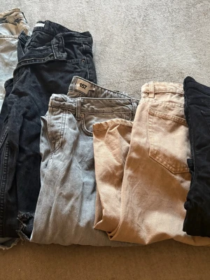 Flerpack jeans i olika färger - Säljer ett paket med flera par jeans i olika färger: ljusblå, svart och beige. Några har slitna detaljer och raka ben. Perfekt för dig som vill ha olika stilar att variera mellan. Märket 157 syns på ett par av jeansen.
