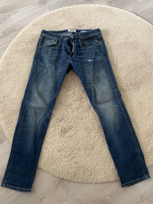Blå slim fit jeans från Replay - Snygga blå slim fit jeans från Replay med klassisk femficksdesign och lätt slitna detaljer framtill. Jeansen har dragkedjegylf och tydliga kontrastsömmar. Perfekta för en trendig och avslappnad look. 
