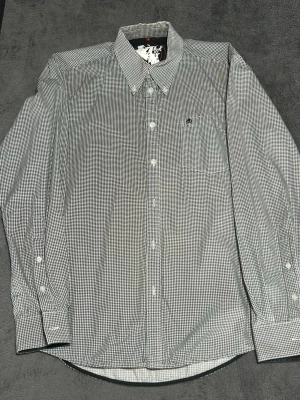 Merc London Shirt – Houndstooth Pattern – Size S - Skjorta från Merc London i klassiskt houndstooth-mönster.  Button down-krage och broderad logga på bröstet. Perfekt för en stilren mod / british casual look.  Detaljer • Merc London • Button down skjorta • Houndstooth / svart-vit • Broderad logga • Storlek S • 100% bomull  📦 Skickas snabbt 💬 Hör av dig vid frågor