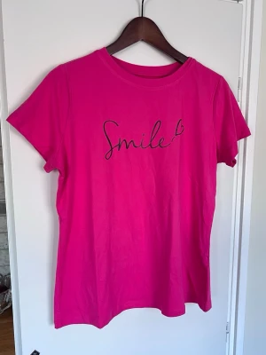 Rosa t-shirt med tryck, storlek L  - Snygg rosa t-shirt med svart texten 'Smile'. Perfekt färgklick! Använd ett par gånger.