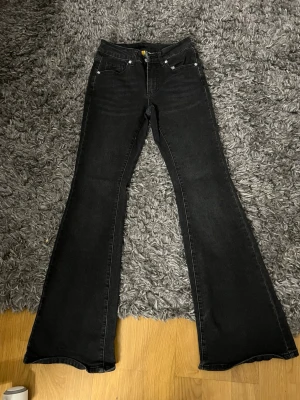 Svarta bootcut jeans med hög midja - Säljer ett par svarta bootcut jeans med hög midja och klassisk femficksmodell. Jeansen har utsvängda ben och är tillverkade i ett stretchigt denimtyg som sitter snyggt. Perfekta för dig som gillar en retroinspirerad look.
