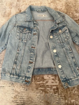 Ljusblå jeansjacka Your Denim - Ljusblå jeansjacka från Your Denim Your Rules med klassisk design, två bröstfickor med knappar och silverfärgade knappar framtill. Snygga sömdetaljer och cool vintage-look. Perfekt att slänga över en hoodie eller t-shirt.