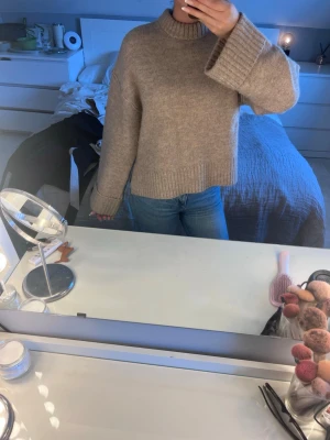 Beige stickad tröja Gina Tricot - Mysig beige stickad tröja från Gina Tricot med hög krage och breda ärmar. Tröjan har en rak passform och ribbstickade detaljer vid hals, ärmslut och nederkant. Perfekt för kalla dagar och enkel att styla till jeans.