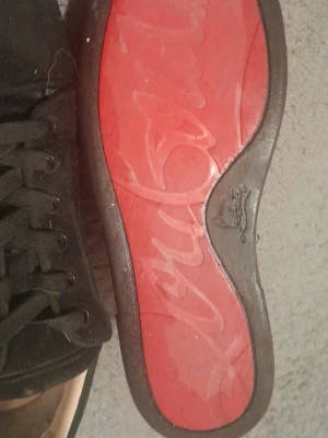 Svarta sneakers från Christian Louboutin - Snygga svarta sneakers från Christian Louboutin i mocka med klassisk röd sula och svarta skosnören. Låg modell med diskret design och exklusiv känsla. Perfekta för dig som vill ha något stilrent men ändå lyxigt. Använda några gånger därav priset men det är inget fel på dom det är bara lite smuts på sulan som går att tvätta bort lätt 