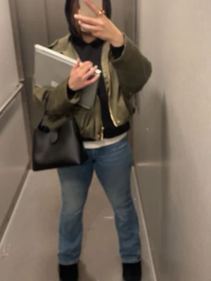 Olivgrön bomberjacka med dragkedja - Säljer en olivgrön bomberjacka med guldig dragkedja framtill. Jackan har en croppad passform och långa ärmar. Perfekt till jeans och hoodie för en avslappnad streetstyle-look.