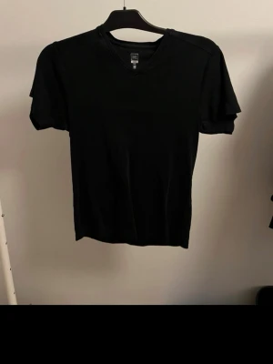 Svart basic t-shirt med v-ringning - En stilren svart t-shirt från Smog med v-ringad hals och korta ärmar. Tillverkad i mjuk bomull som känns skön mot huden. Perfekt till jeans eller shorts för en enkel och clean look.